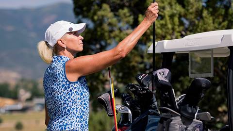 Woman selects golf club from golf cart