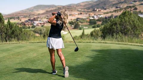 Woman swings club at golf ball on sunny day