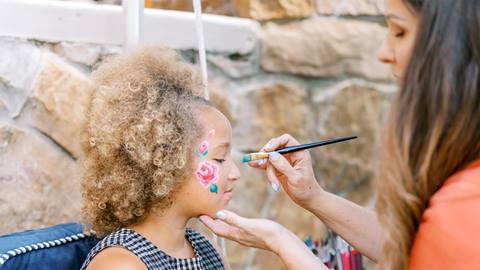 Woman painting flowers on young girl's face