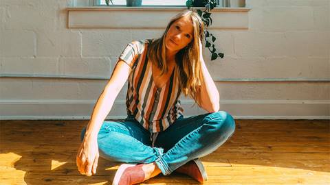 Singer, Alicia Stockman, smiling for a photo while sitting cross-legged on the floor.