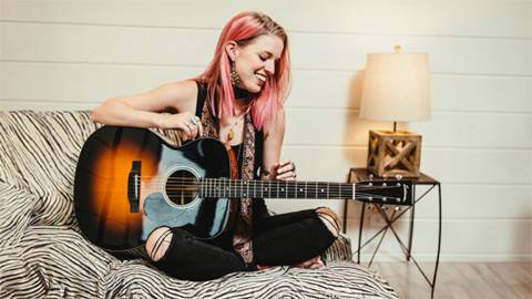 Musician, Aspen Anonda, sitting cross-legged while playing a guitar.