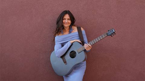 Musician, Shannon Runyon, leaning against a wall, while holding her guitar.