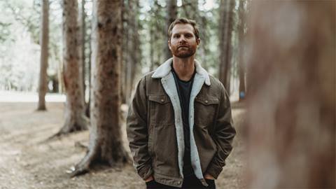 Musician, TJ Gurn, standing in the woods looking directly at the camera.