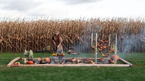 Chef Sarah Glover is preparing a dinner in the middle of a field in a fire pit.