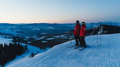 Deer Valley Ski Patrol team members in uniform standing at the edge of a ski run.