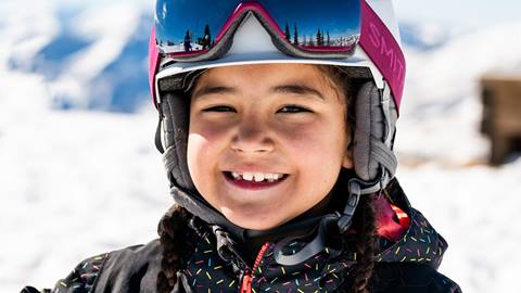 Young girl wearing black jacket and pink goggles smiling