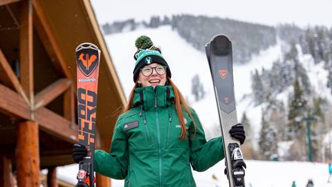 Female Deer Valley staff member carrying guests skis.