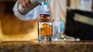 Bartender adding smoke to a whiskey cocktail.