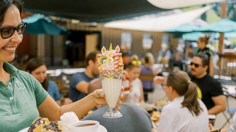 Deer Valley staff member holding unicorn milkshake on the Royal Street Cafe deck during the summer.