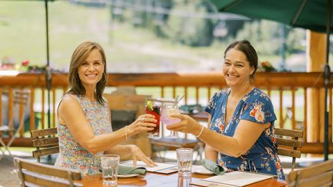 Two women clinking glasses on the Royal Street Cafe deck during the summer.