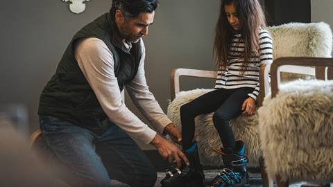 Grandpa helping granddaughter with ski boots inside Deer Valley lodging property.