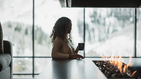 Woman enjoying coffee by fire in Deer Valley lodging property.