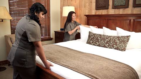 Two housekeepers make a bed in a private residence.