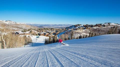 Guest wearing pink jacket is skiing a groomed run towards Silver Lake Village.