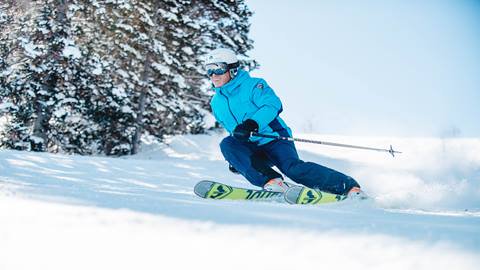 Deer Valley guest wearing blue ski jacket skiing on bluebird day.