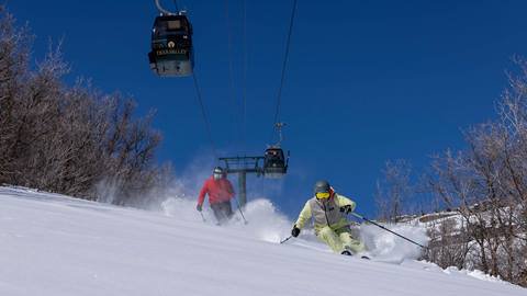 Two guests skiing powder under Jordanelle Express Gondola.