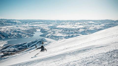 Man skiing a groomed run with view of the Jordanelle Reservoir.