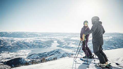 Skiers talking on ski run with view of Jordanelle Reservoir.