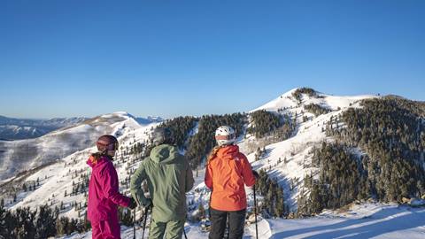 Three skiers standing in Deer Valley's expanded terrain with a view of the mountains.