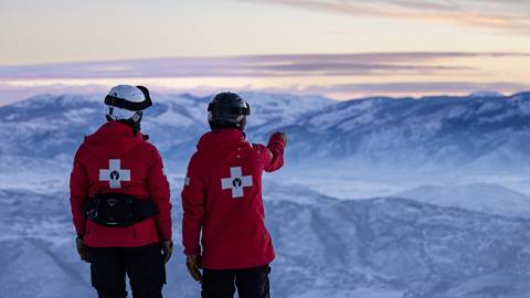 Two Deer Valley Ski Patrol standing on the mountain at sunrise.