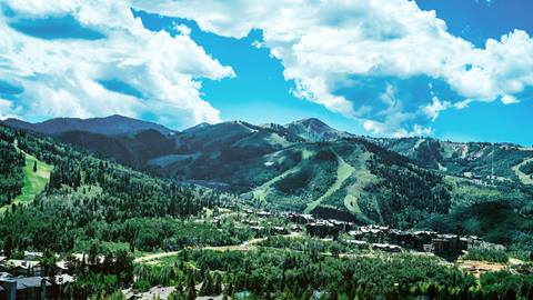 Vibrant summer mountain scene at Deer Valley Resort, with a bright bluebird sky and luxurious properties in the foreground.