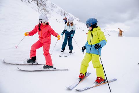 Three young skiers glide down a snowy slope.