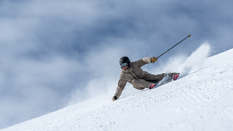 A skier on Premium Skis carves down a snowy slope, kicking up snow