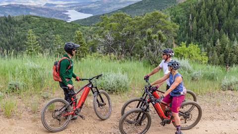 Two guests talking to their bike guide at Deer Valley with the Jordanelle Reservoir in the background